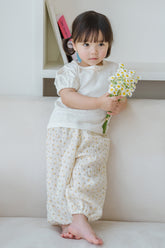 Toddler girl standing in Avauma Breeze Jogger Pants, yellow flower design, holding white flowers.